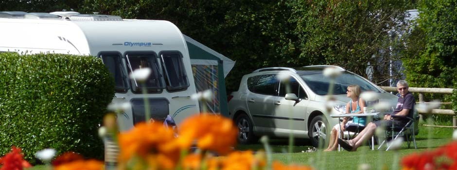 couple sat outside a caravan and awning on pitch 60 with orange flowers in foreground