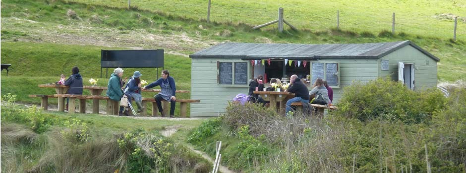 people sat outside the Hidden Hut at Porthcurnick beach, Portscatho