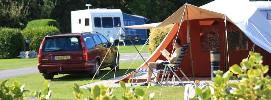 gentleman sat reading in the sunshine outside a tent on pitch 53