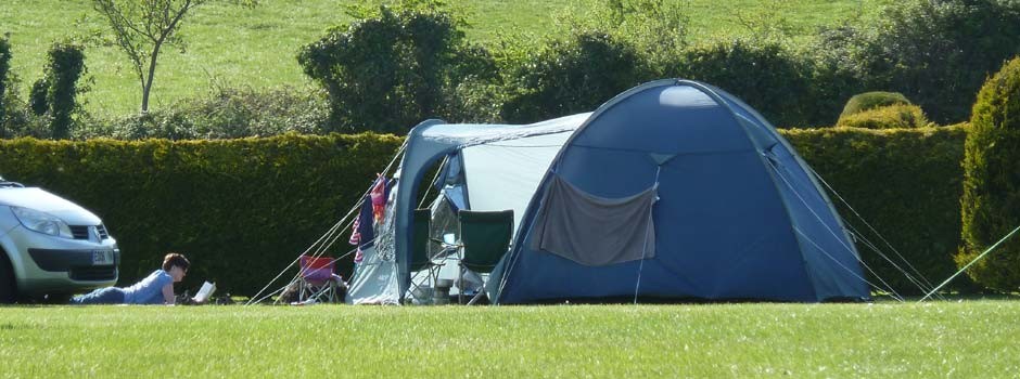 woman reading laid on the grass outside a tent on pitch 43