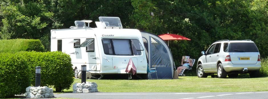 woman reading sat outside a caravan and awning on pitch 22